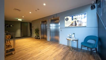 Un hall d’hôtel avec un sol en bois, un mur bleu, un ascenseur, un comptoir d’accueil et une chaise.