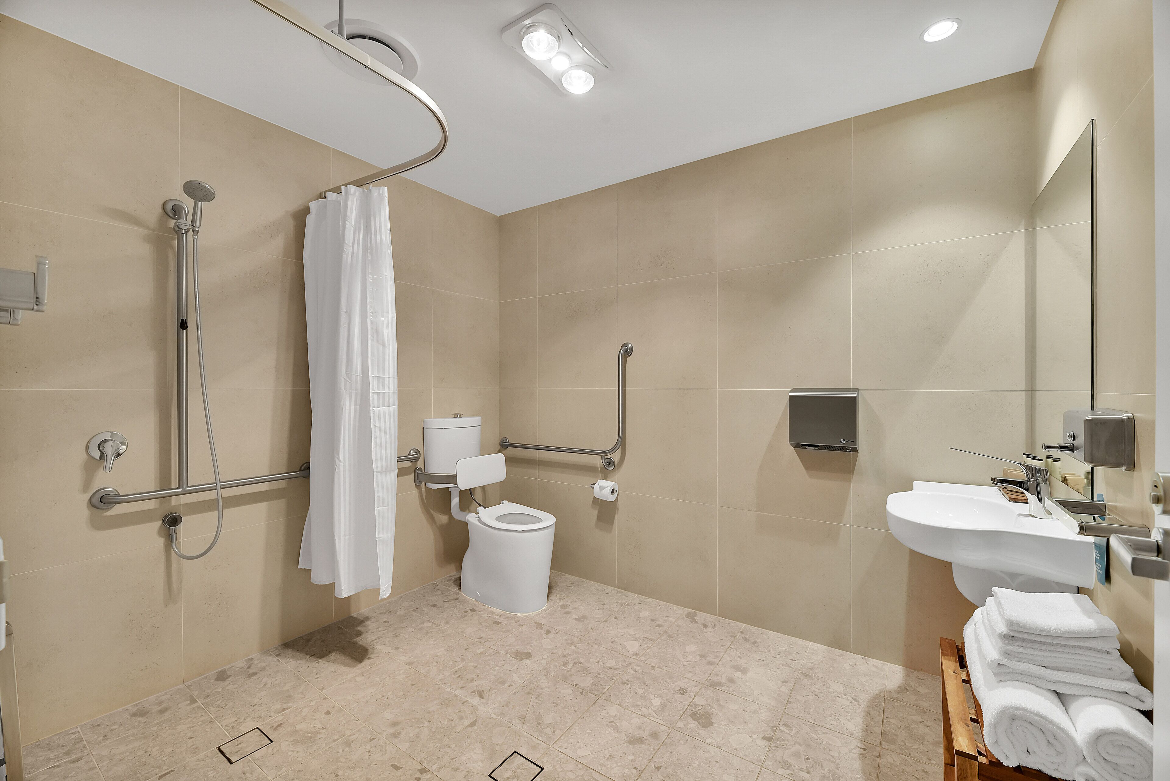 Et moderne badeværelse med bruser, toilet og håndvask, udstyret med gelændere og en håndtørrer.