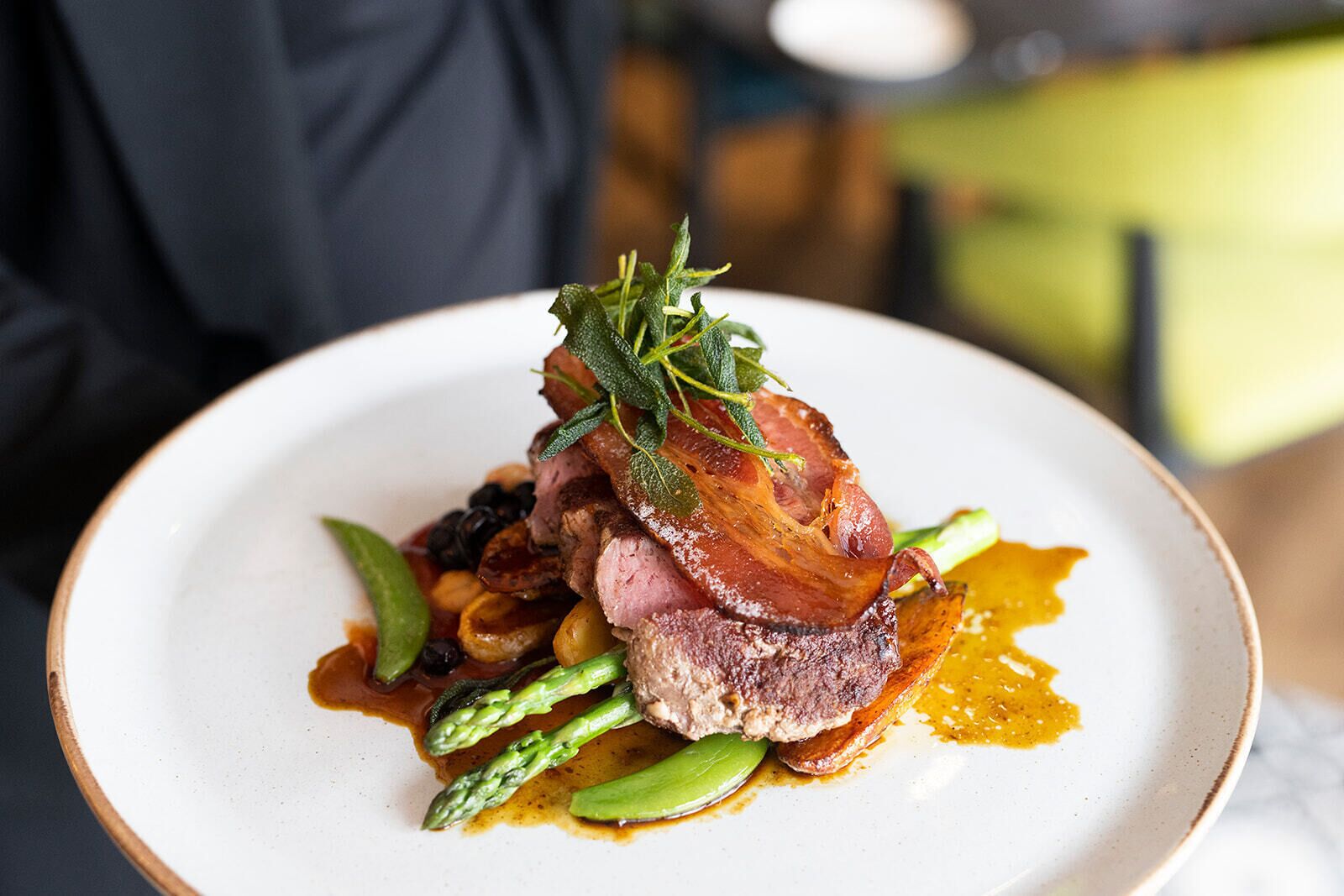 A plate of food with a piece of meat, asparagus, and a garnish.