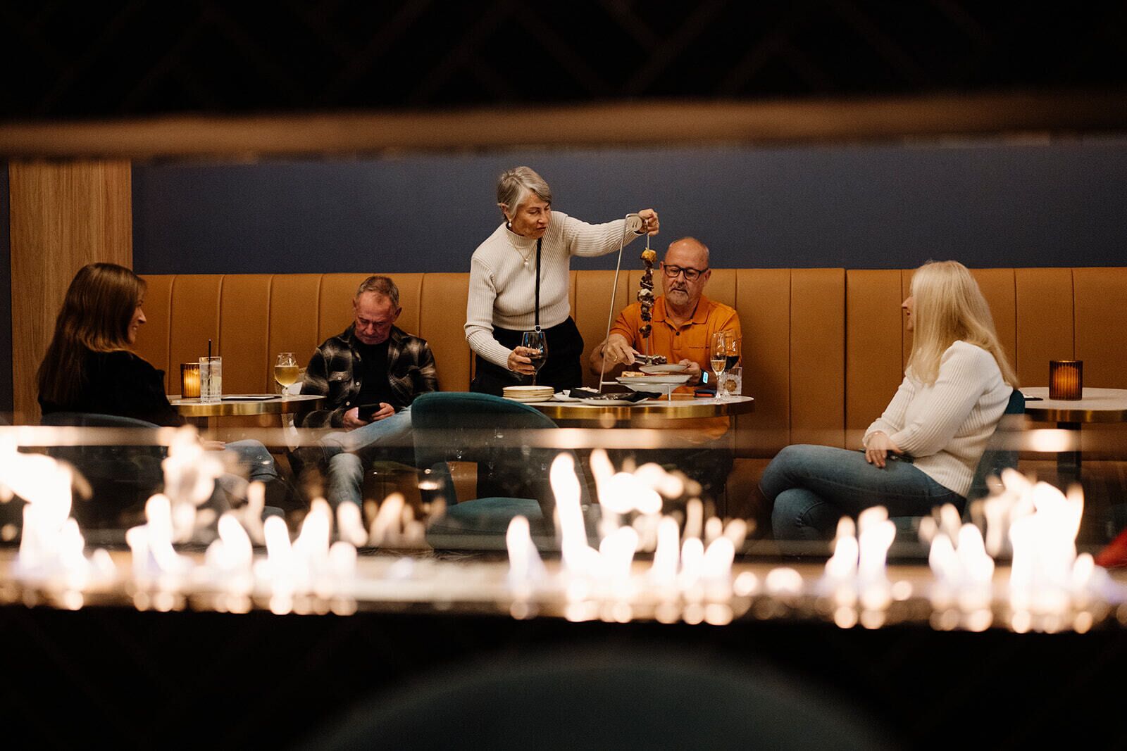Un groupe de personnes est assis autour d’une table dans un restaurant au décor intérieur moderne, comprenant des panneaux de bois et une cloison en verre.