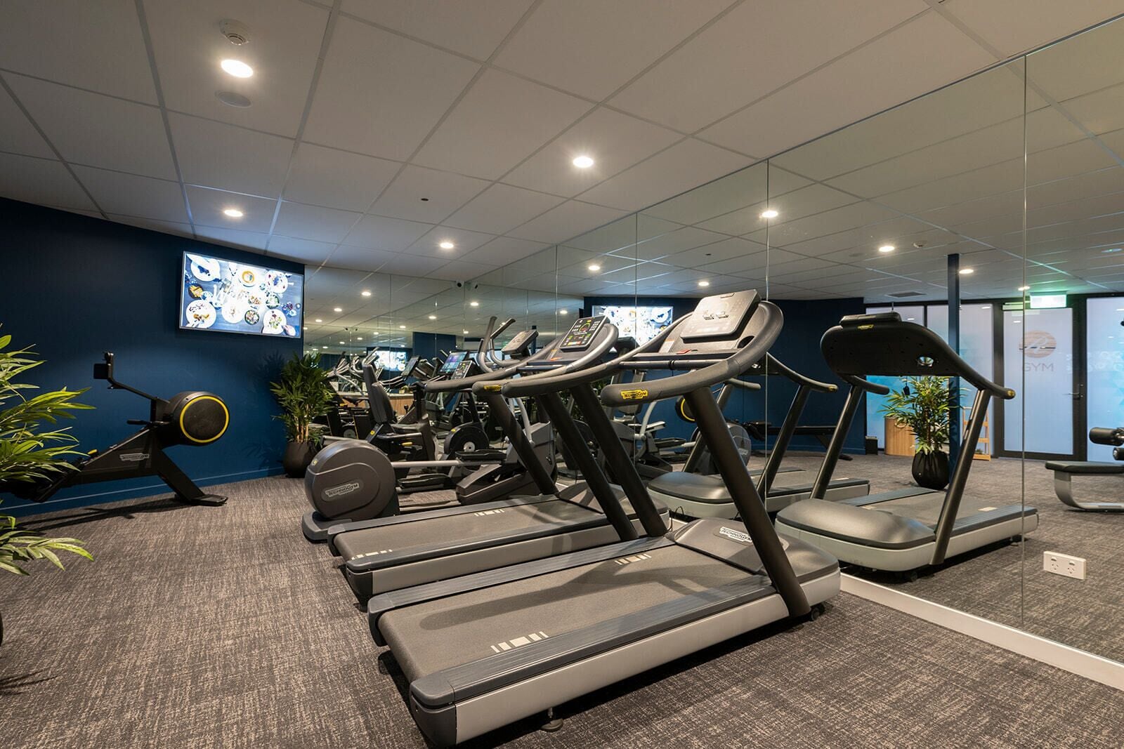 Een fitnessruimte met loopbanden, hometrainers en roeiapparaten.