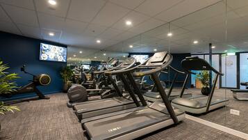 Een fitnessruimte met loopbanden, hometrainers en roeiapparaten.