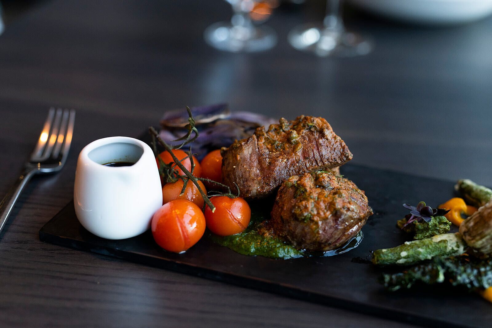 A plate of food with meat, tomatoes, and a small bowl of sauce.