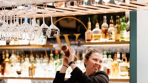 A bar area with shelves of liquor bottles and a person holding a bottle. - The Remington Orange (Orange)