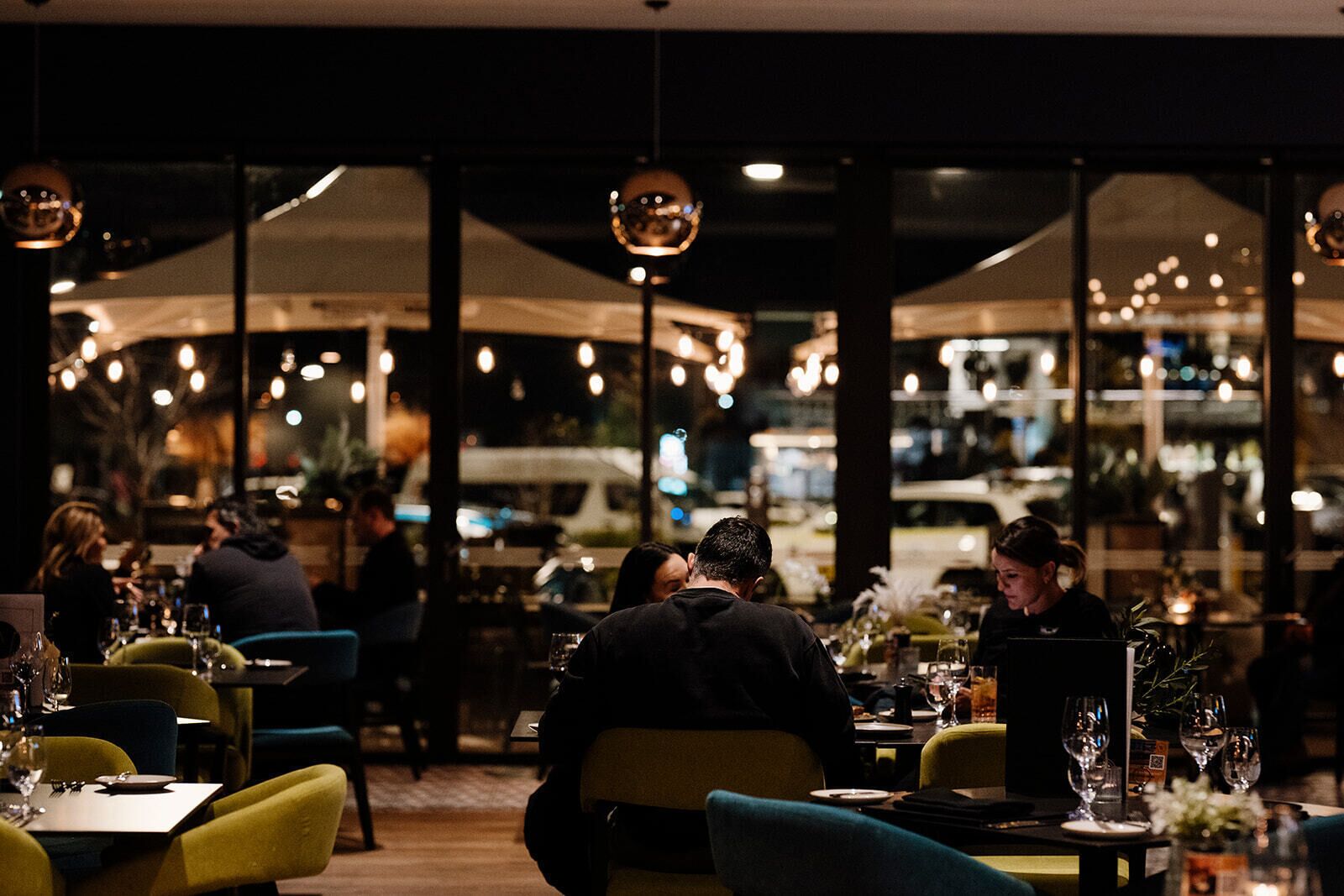 Un espace de restauration intérieur avec des tables disposées pour accueillir plusieurs personnes, de grandes fenêtres et des luminaires suspendus.