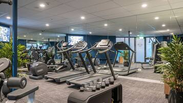 A gym with treadmills, ellipticals, and weight machines, carpeted flooring, and potted plants.