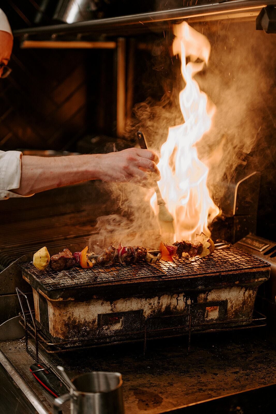 Un chef cuisant de la viande sur un barbecue au charbon de bois, avec des flammes apparentes.