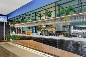 Un bar moderno con barra, taburetes y una variedad de botellas y vasos.