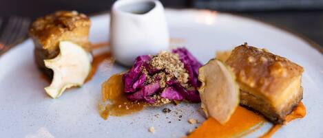 Un plato con un trozo de carne, una guarnición de col morada y una taza blanca pequeña.