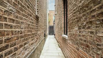 A narrow alleyway with brick walls and a tiled floor, leading to a gate.