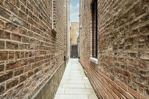 Un estrecho callejón con paredes de ladrillo y suelo de baldosas, que conduce a una puerta.