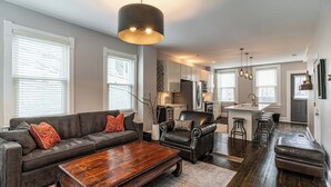A modern living room with a sofa, coffee table, and a dining area with stools. - Private Historic Coach House Wicker Park (Chicago)