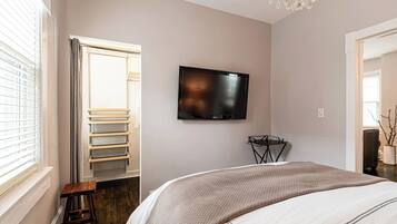 A bedroom with a bed, a TV mounted on the wall, a small table, and a chair.