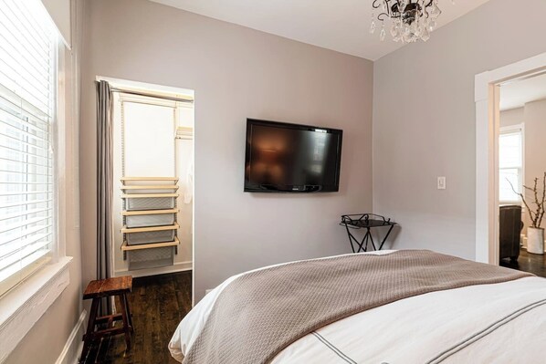Un dormitorio con cama, televisor montado en la pared, una mesita y una silla.
