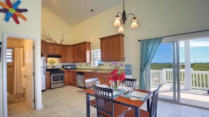 Una cocina amplia con armarios de madera, un comedor con mesa preparada para cuatro personas, y un balcón con vistas al paisaje.