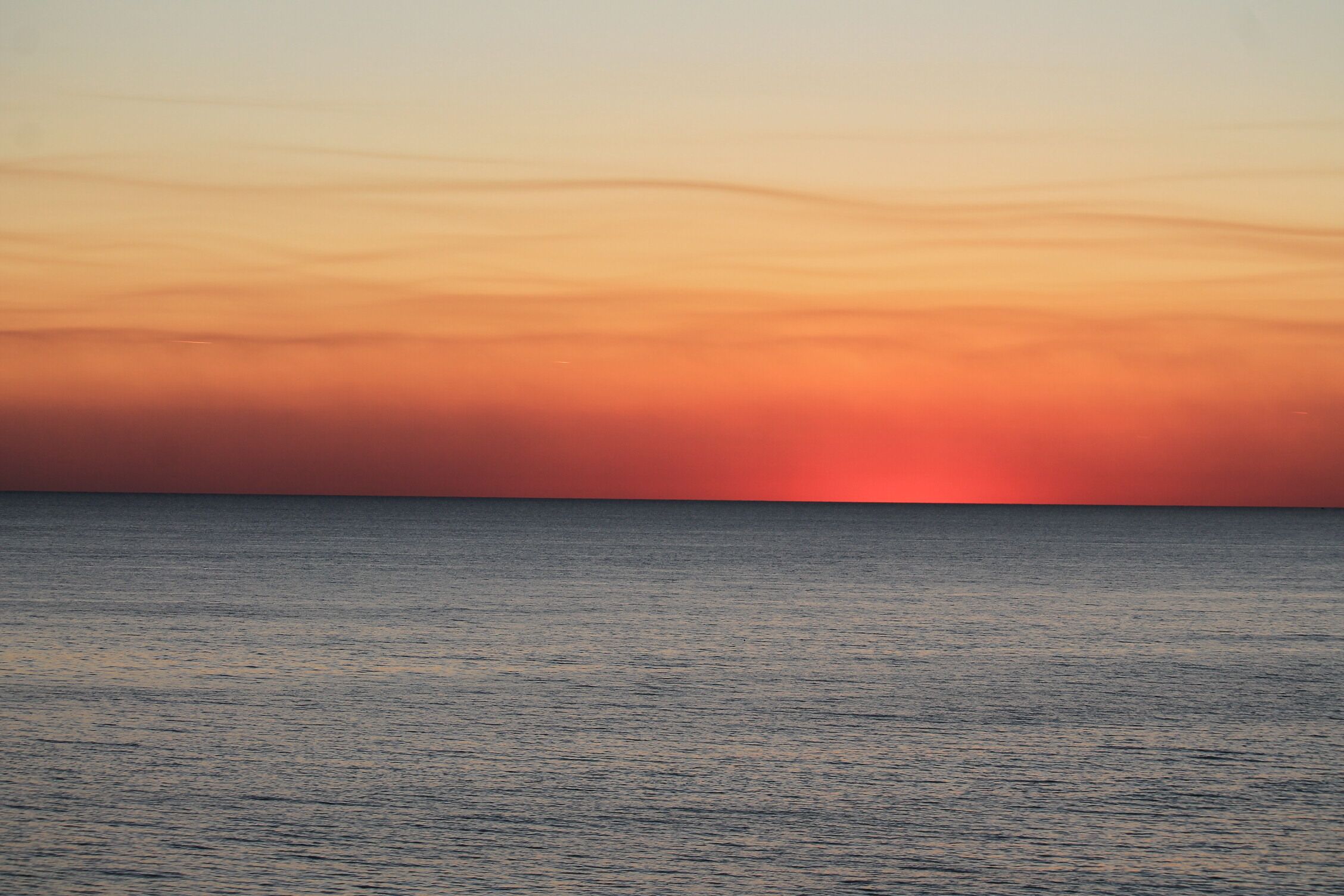 Ein Sonnenuntergang über einem ruhigen Meer mit klarem Horizont.