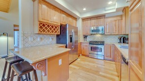 A kitchen with wooden cabinets, a stainless steel refrigerator, a microwave, an oven, and a bar stool. - Central Townhome < 1 Mi to The Village at Mammoth! (Mammoth Lakes)