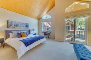 Ein Schlafzimmer mit einem großen Bett, einem Schreibtisch, einem Stuhl und einem Balkon mit Blick auf eine Holzhütte.