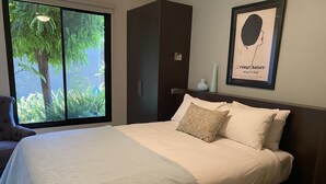 A neatly made bed with a floral pillow, a chair, and a large window with a view of greenery. - Adelphi 3 - River views located in the centre of Echuca (Echuca)