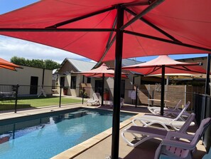 Un espace piscine agrémenté de parasols rouges, de chaises longues et d’un jardin clos.