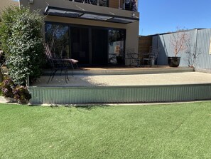 Une terrasse extérieure moderne comprenant un espace repas, un petit jardin et une grande porte-fenêtre coulissante donnant sur un espace intérieur.