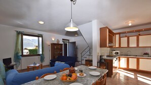 A dining area with a table set for four, a blue sofa, a fruit bowl, and a view of mountains through a window. - Belvedere A (Colico)