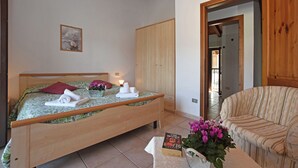 A bedroom with a wooden bed, a bedside table with a book and flowers, a wooden wardrobe, and a sofa. - Belvedere A (Colico)