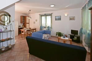 A living room with a sofa, dining table, chairs, a TV, and a kitchen area with cabinets and a refrigerator.