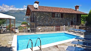 A stone building with a swimming pool, outdoor seating, and a view of mountains. - Belvedere A (Colico)