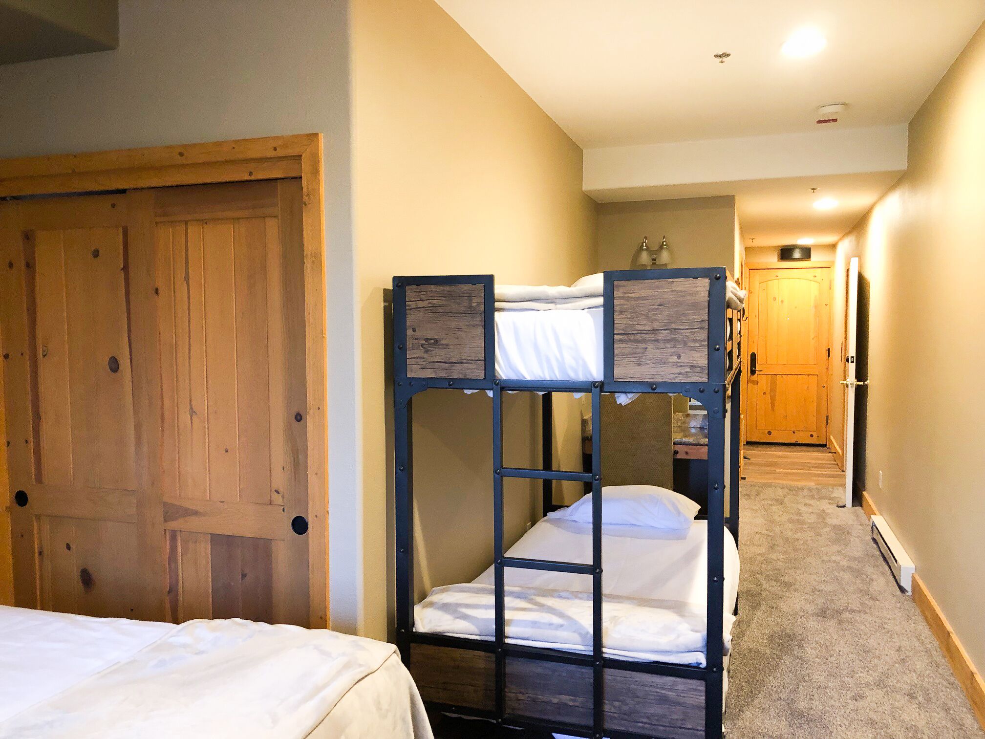 A room with bunk beds, a wooden door, and a hallway leading to another room.