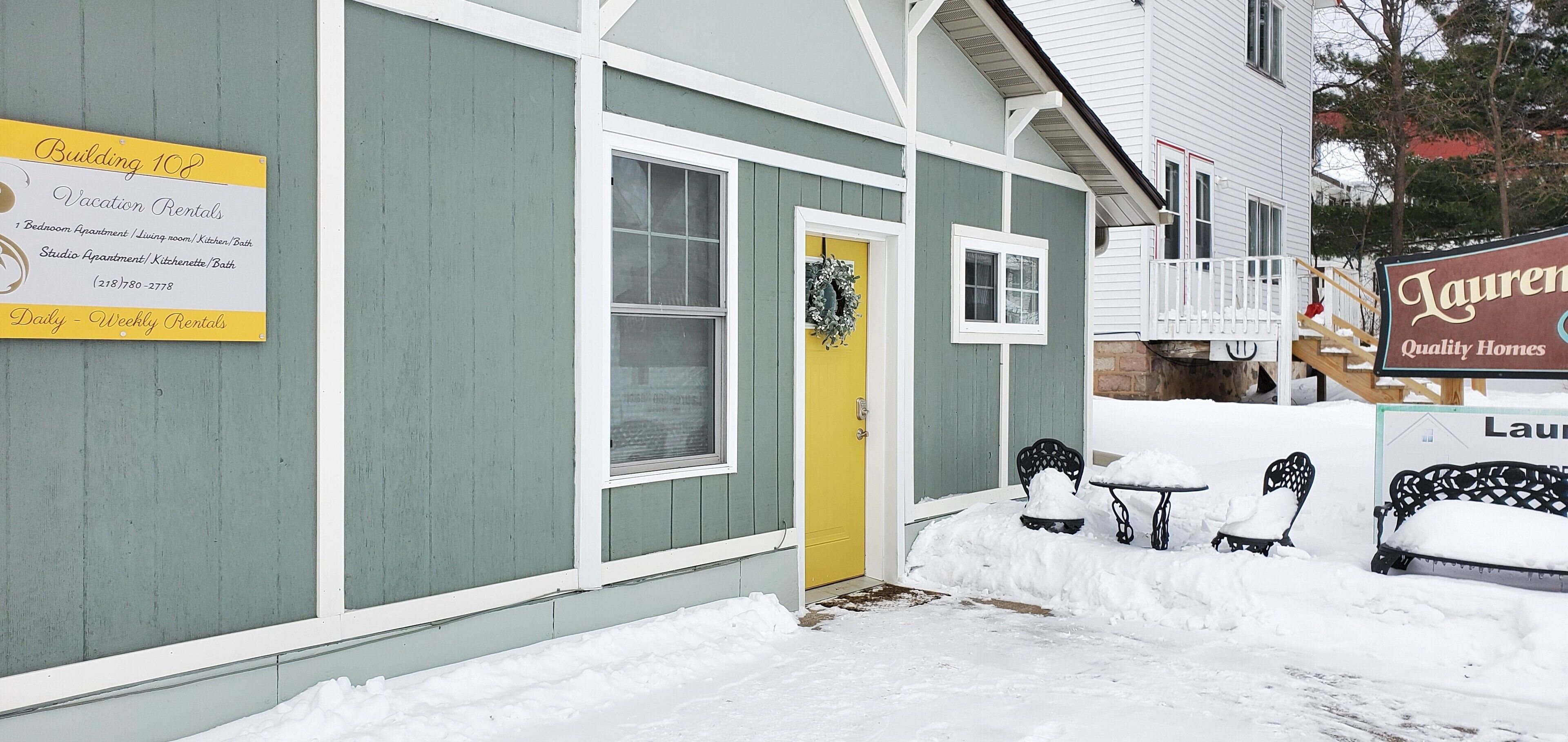 A building with a sign for vacation rentals, a yellow door, and snow-covered benches.