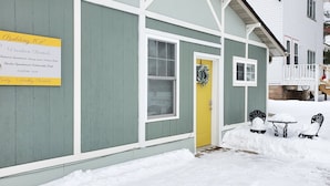 Un immeuble avec une enseigne indiquant qu’il propose des locations de vacances, une porte jaune et des bancs couverts de neige.