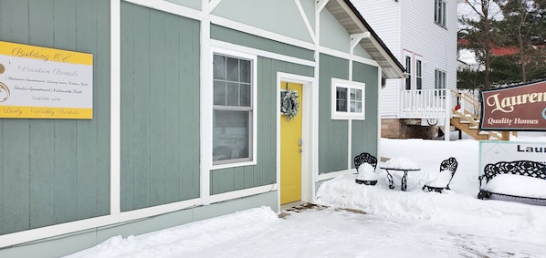 A building with a sign for vacation rentals, a yellow door, and snow-covered benches.