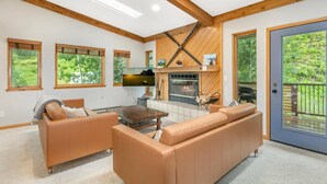 Ein modernes Wohnzimmer mit Kamin, Ledersofas und großen Fenstern mit Blick auf Grünflächen.
