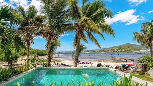 A pool area with palm trees, a view of the sea, and lounge chairs.