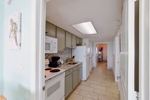 Kitchen with central island, sink, microwave, and refrigerator, leading to a hallway.