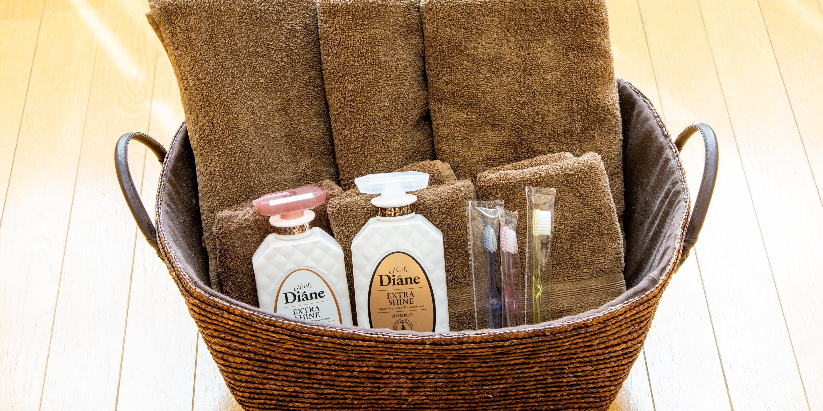 A wicker basket containing brown towels, two bottles of Diane Extra Shine Shampoo, and a toothbrush.