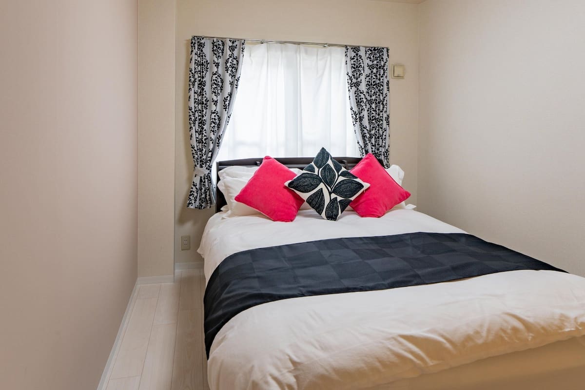 Cama bem arrumada com colcha quadricula preta e branca, duas almofadas com padrão preto e branco e uma almofada branca.