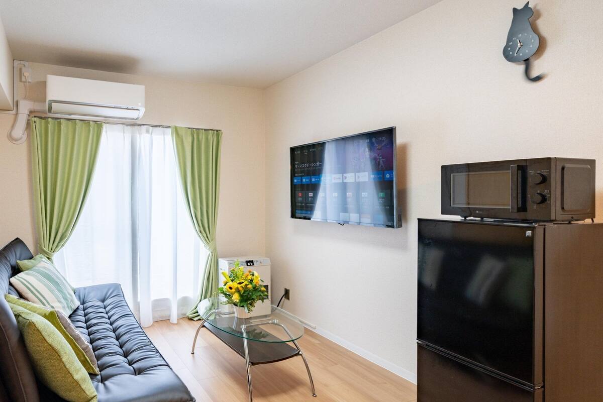 Uma sala de estar moderna com sofá, mesa de centro de vidro, TV de tela plana, micro-ondas e ar condicionado.