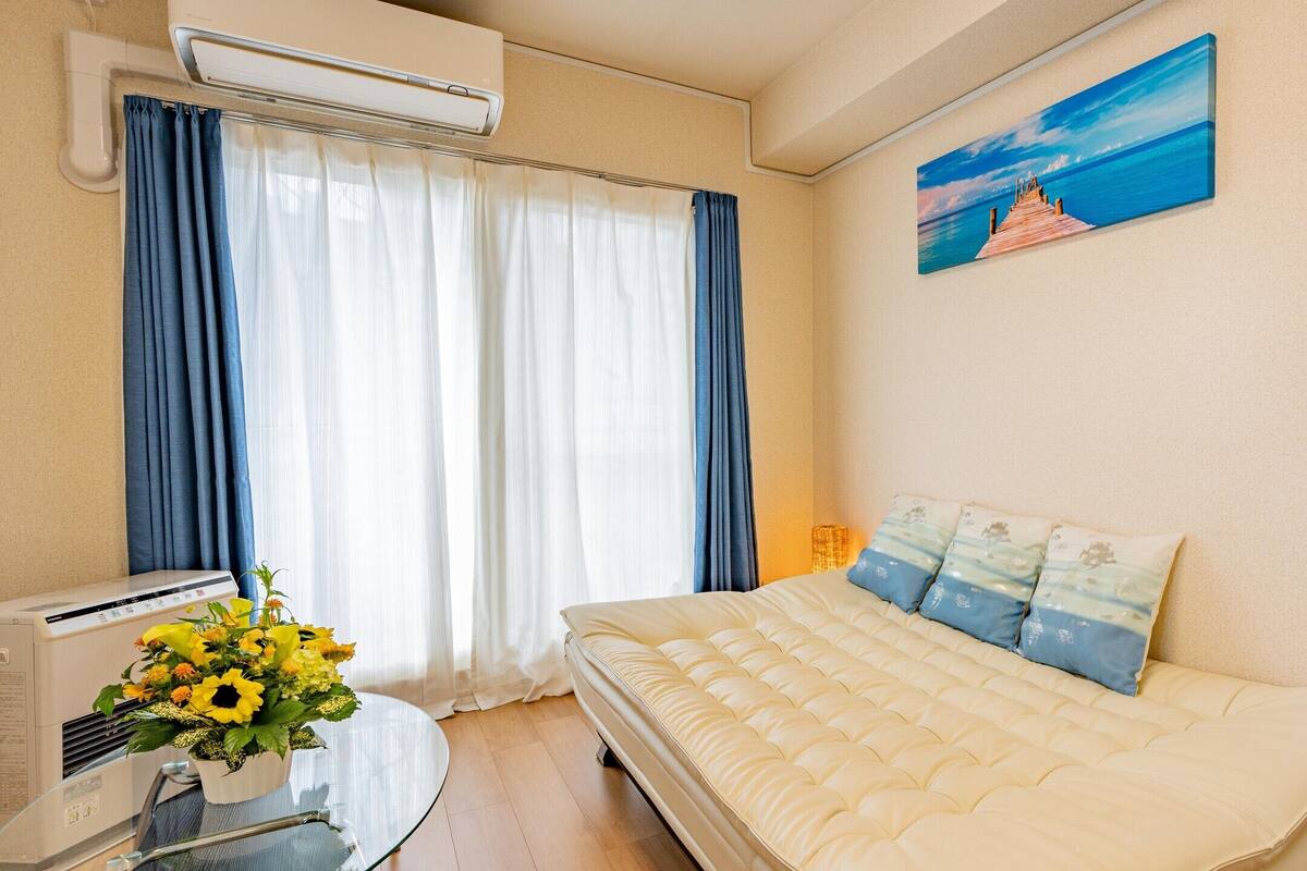 Quarto de hotel com cama, ar condicionado, cortinas, um quadro e um vaso de flores.
