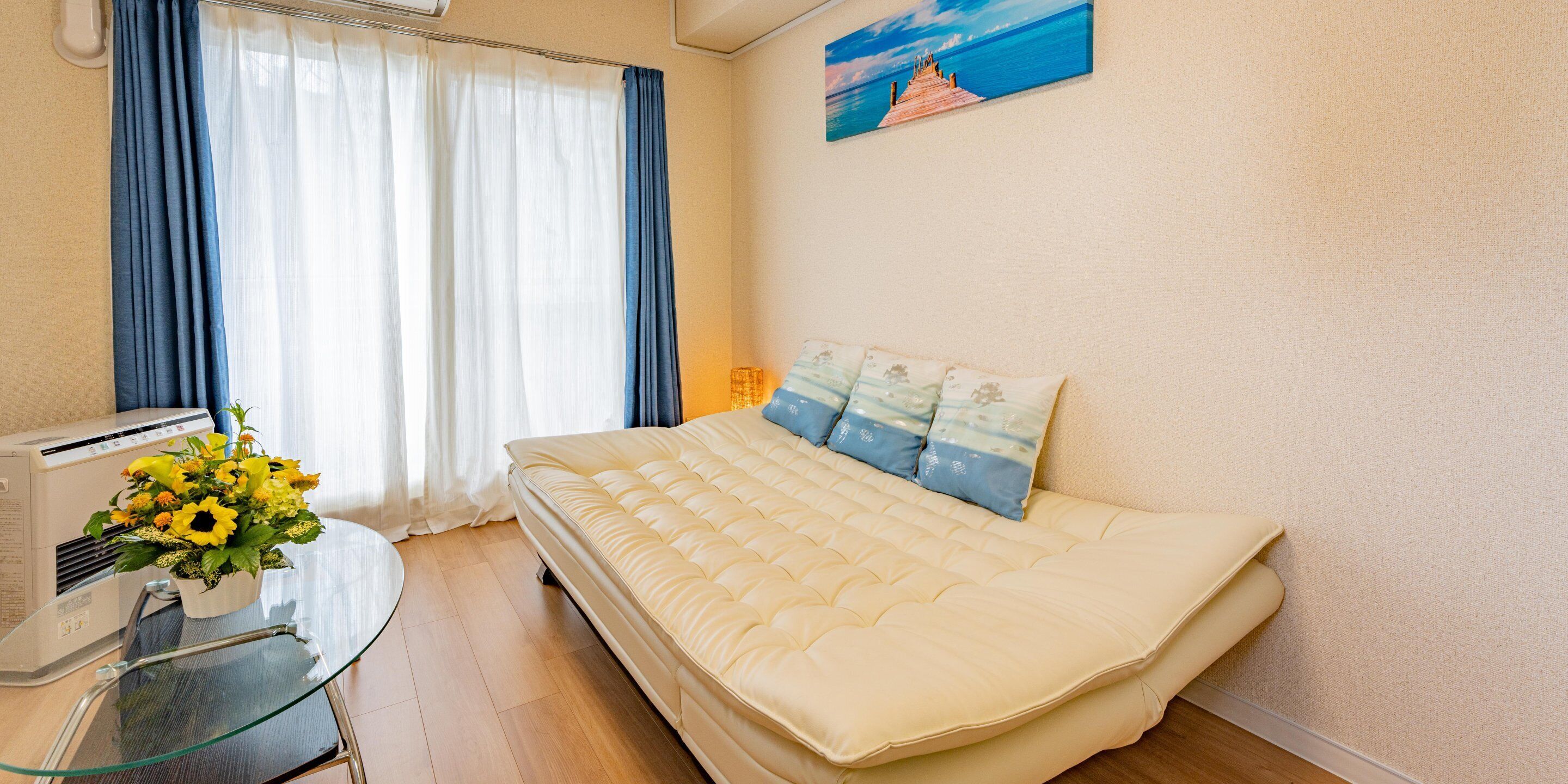 Ein Schlafzimmer mit einem Bett, einem Glastisch mit Blumenvase, einem Heizgerät und einem Bild an der Wand.