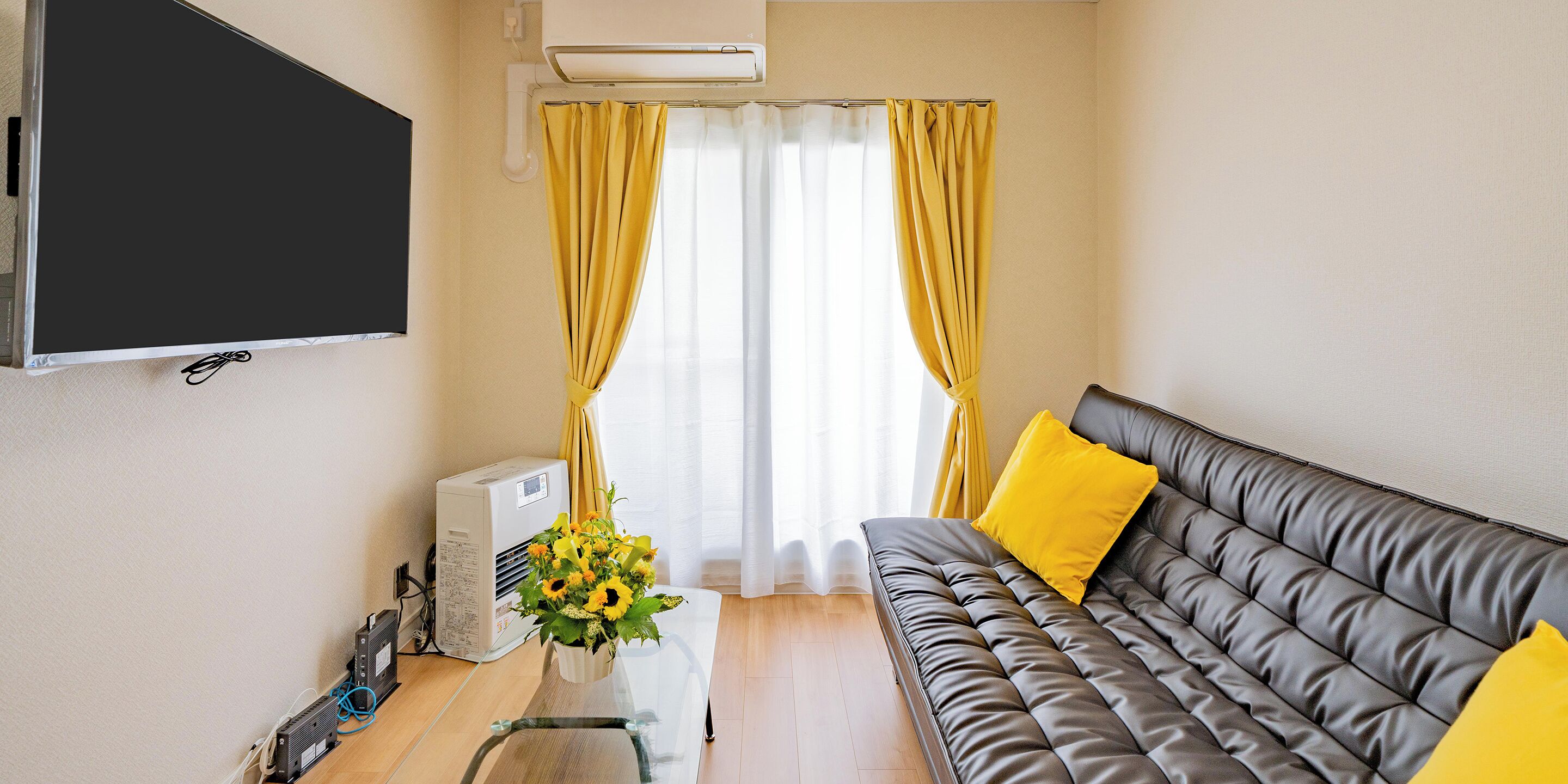 A living room with a sofa, a flat-screen TV, an air conditioner, and a window with curtains.