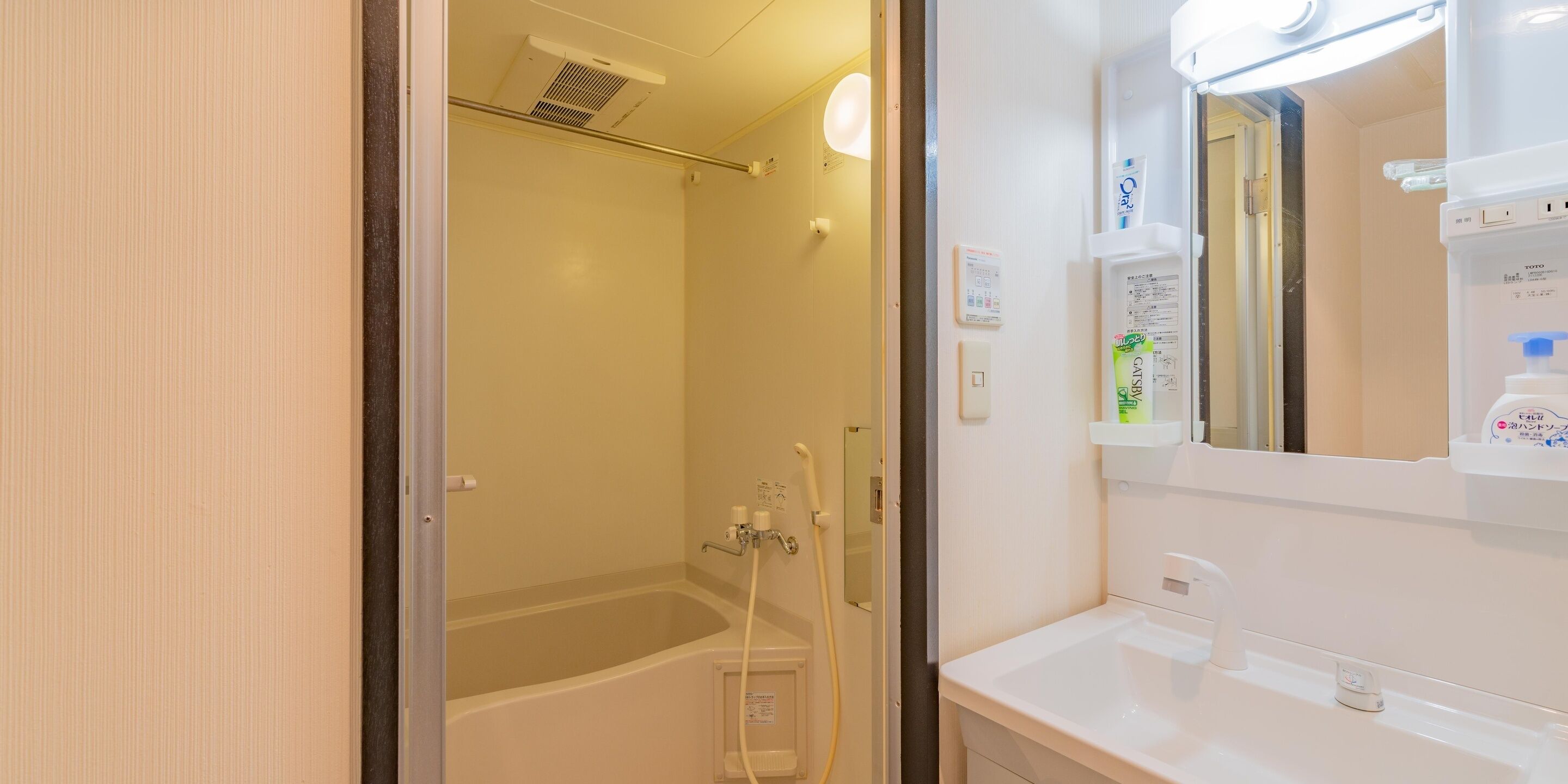 Un baño con bañera, lavamanos, espejo y estante con artículos de aseo.