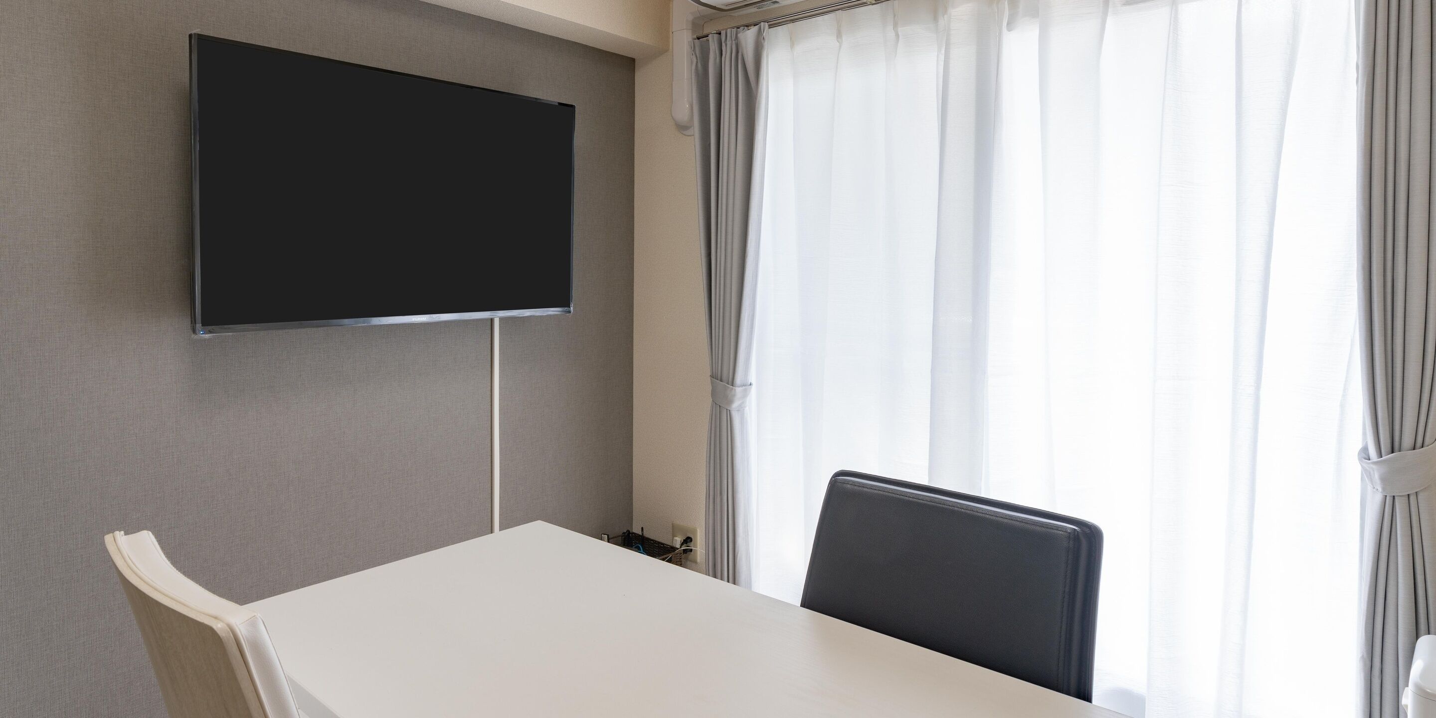 A conference room with a flat-screen TV mounted on the wall, a white table, and a black chair.