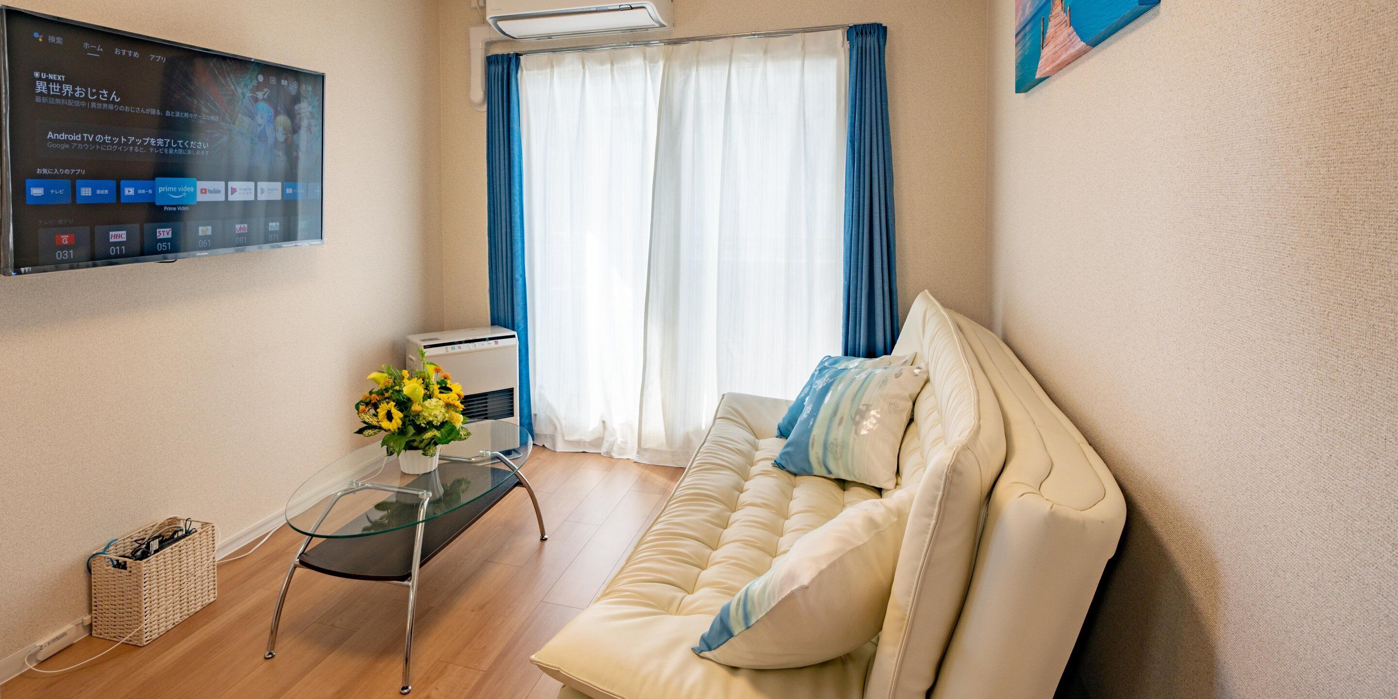 Ein modernes Wohnzimmer mit einem beigen Sofa, einem Glastisch und einem an der Wand befestigten Flachbildfernseher, der eine digitale Benutzeroberfläche zeigt.