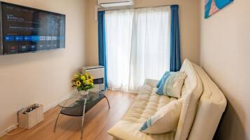 Ein modernes Wohnzimmer mit einem beigen Sofa, einem Glastisch und einem an der Wand befestigten Flachbildfernseher, der eine digitale Benutzeroberfläche zeigt.