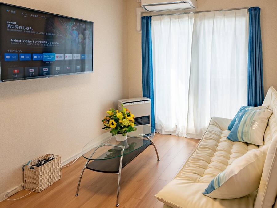Ein modernes Wohnzimmer mit einem beigen Sofa, einem Glastisch und einem an der Wand befestigten Flachbildfernseher, der eine digitale Benutzeroberfläche zeigt.