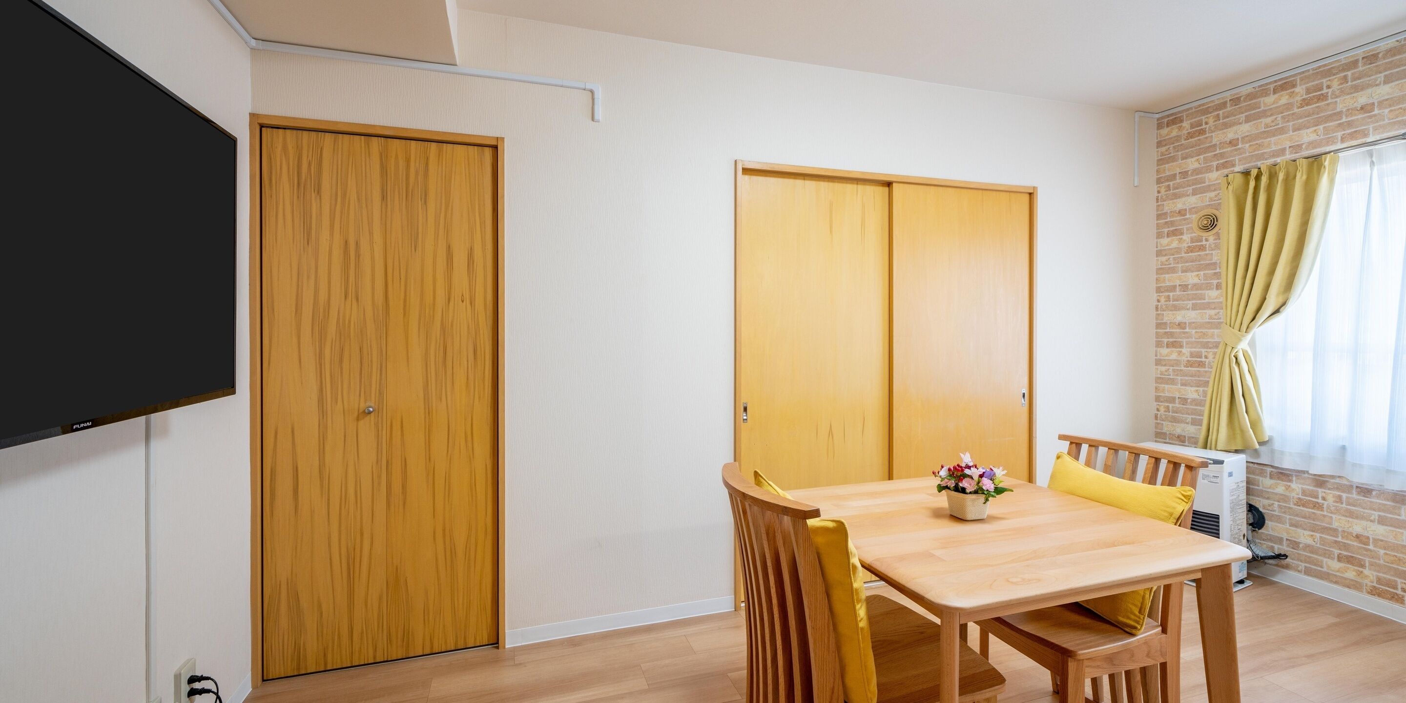 Una habitación con una mesa de comedor de madera, sillas, un televisor y una pared de ladrillo.