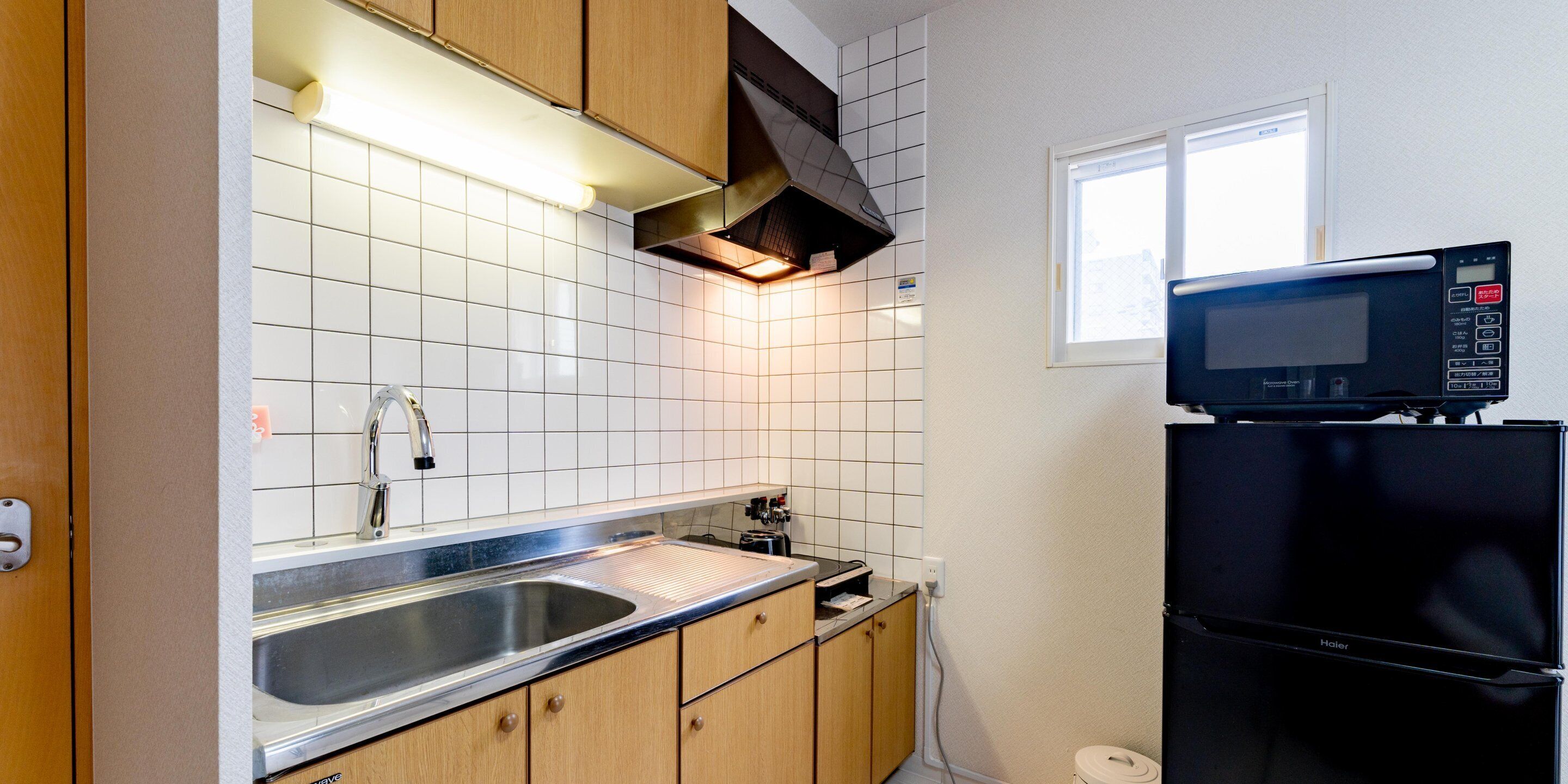 A compact kitchen with a stainless steel sink, wooden cabinets, a black refrigerator, and a microwave.