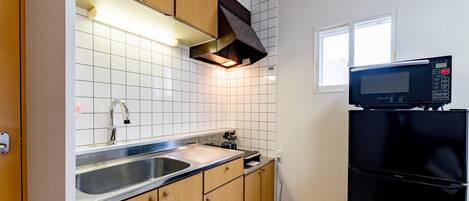 A compact kitchen with a stainless steel sink, wooden cabinets, a black refrigerator, and a microwave.